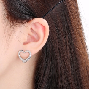 Gros plan de boucles d'oreilles cœur creux en argent portées par un mannequin de mode
