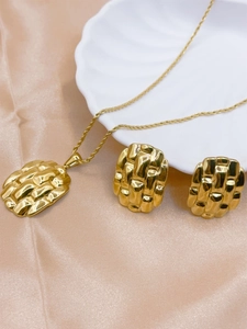 Detail of square woven texture gold pendant and earrings on pink satin with a shell plate