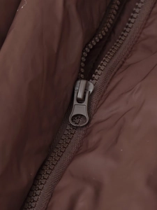 Détail de la fermeture éclair en résine sur une veste d'hiver marron foncé à capuche