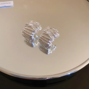 Close-up of silver earrings with irregular wrinkled texture reflecting on a mirror surface