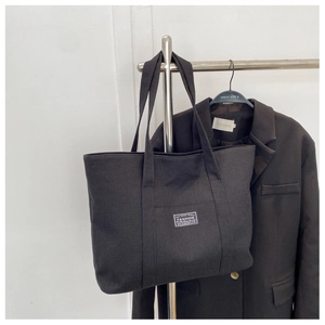 Detail of black canvas tote bag with FASHION label hanging on a metal rack