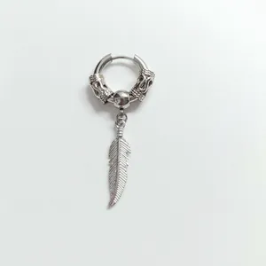 Macro detail of a vintage stainless steel ear clip featuring a carved ring and feather pendant