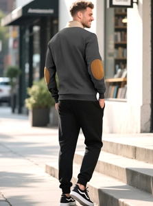 Detail of grey sweatshirt with brown elbow patches and black joggers on a model
