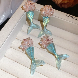 Detail of pink pearl beads and blue iridescent mermaid tail earrings on a gift box