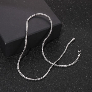 Silver stainless steel woven chain necklace with lobster clasp on textured surface