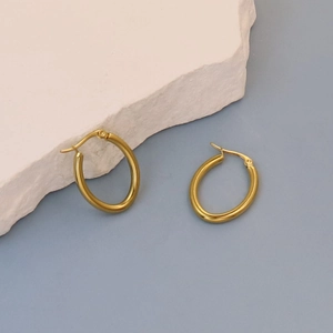 Detail of gold oval hoop earrings with polished metal finish on a stone pedestal
