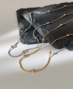 Close-up of gold and silver snake bone necklaces with metal beads on black stone
