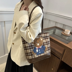 Brown plaid tote bag with embroidered bear and shoulder strap shown on a model