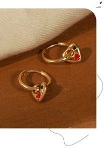 Macro detail of gold plated heart earrings with red and green enamel on wooden surface