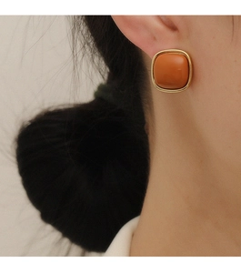 Close-up of a model wearing square geometric orange resin earrings with gold metal frame