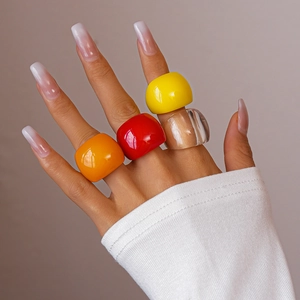 Close-up of chunky resin rings in yellow and red on fingers for a minimalist bold look