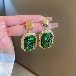 Detail view of vintage green resin heart earrings with gold trim held by hand