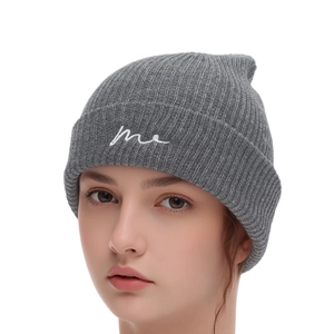 Detail of dark grey ribbed knit beanie featuring white embroidered me script on the cuff
