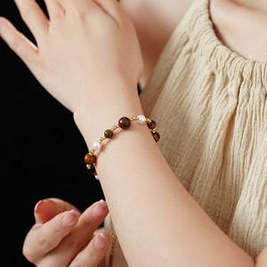 Detail of gold-plated geometric beaded bracelet with tiger eye stones and pearls on wrist