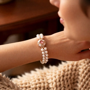 Detail view of a double-strand pearl bracelet with a pink gemstone center and gold finish