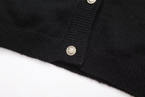 Détail du cardigan en maille noire avec des boutons dorés vintage à motif de blason