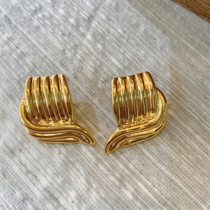 Détail de boucles d'oreilles dorées avec texture rayée sur fond en lin neutre