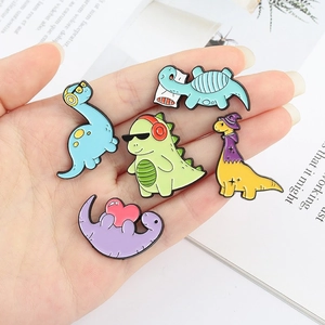 Set of five colorful dinosaur fossil enamel pins displayed on a hand with white background
