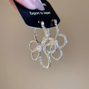 Macro view of silver floral earrings with embossed petals and centered pearl details