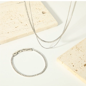Détail d'un collier à double chaîne argentée et d'un bracelet de tennis sur marbre
