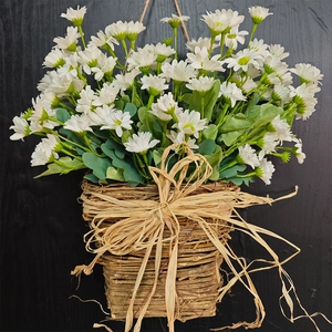 Wall-mounted woven basket with artificial white daisies and a large straw bow tie