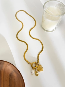 Close-up of gold flat snake chain with pearl, heart, and letter S letter charms