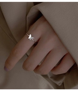 Primo piano di un anello a farfalla d'argento indossato al dito su sfondo beige