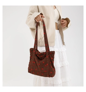 Detailed texture of brown corduroy tote bag with embroidered red strawberry patterns