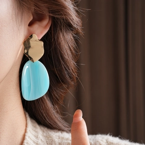 Gros plan sur des boucles d'oreilles dorées en métal avec gouttes de résine bleu ciel