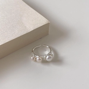Anillo abierto de plata S925 con tres perlas elegantes sobre un libro beige