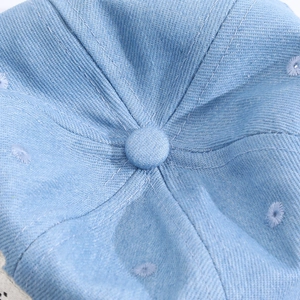 Détail du haut d'une casquette en denim bleu clair avec œillets brodés et bouton central