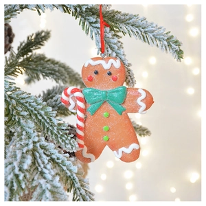 Close-up of clay gingerbread man ornament hanging on a snowy Christmas tree branch