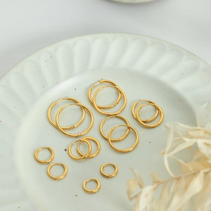Golden titanium steel hoop earrings set in various sizes on white ceramic tray