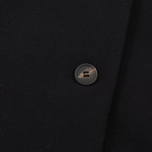 Détail de la texture laineuse et du bouton marbré sur un manteau court noir minimaliste