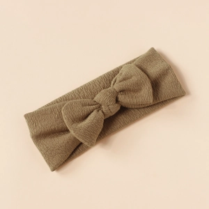 Detail of khaki knitted baby headband with a large textured bow on a plain background