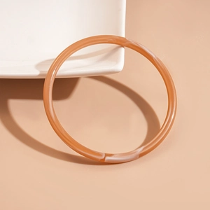 Close-up of amber brown acrylic bangle with white marble swirl on a ceramic dish