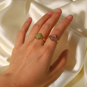 Close-up of gold oval gemstone rings in green and purple on model's hand with silk