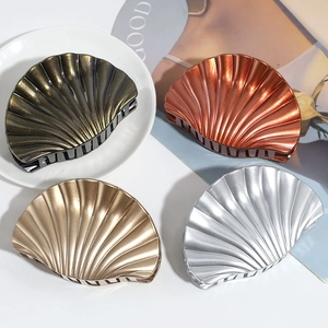 Shell-shaped hair claw clips in black, bronze, gold, and silver finishes displayed on a table