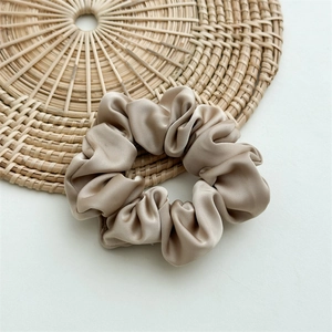 Detailed view of champagne satin scrunchie with soft silk texture on a woven mat
