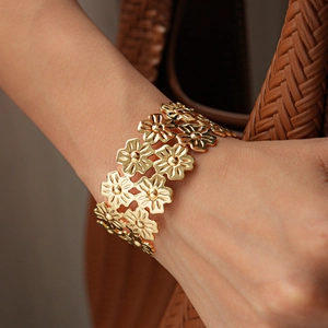 Detailed close-up of a wide gold metal open cuff bracelet featuring hollow floral patterns