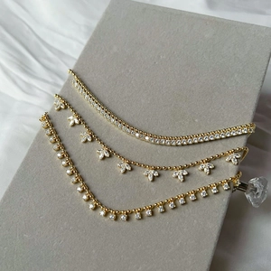 Detailed view of three gold leaf necklaces and zircon chains on a grey jewelry stand