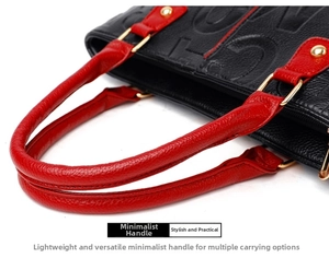 Detail of red leather handles on a black embossed handbag with gold hardware accents