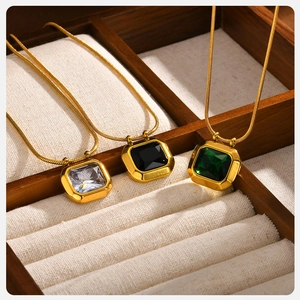 Detail of square zircon pendants in white, black and green on gold snake chain
