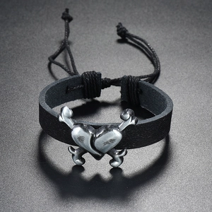 Macro view of woven black leather bracelet with silver crossbone heart detail and adjustable cord
