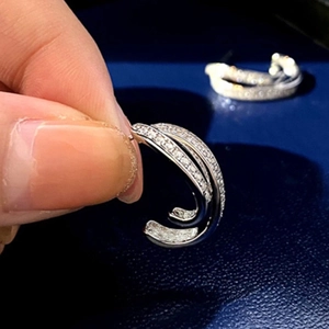 Close-up of silver irregular pavé huggie hoop earrings held in hand against blue background