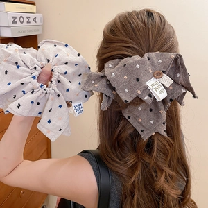 Close-up of beige polka dot fabric scrunchie and large bow hair clip in a warm home setting