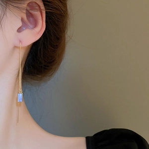 Detailed close-up of a long golden chain earring with a shimmering blue square pendant