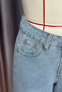 Gros plan d'un jean large bleu clair montrant la taille et les surpiqûres orange contrastées
