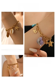 Detail of gold chain bracelet with sea star, turtle, fish, and shell charms on model wrist