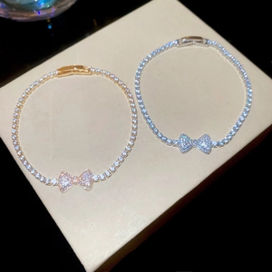 Macro shot of silver and gold bow pendants with zircon pavé setting on fine bracelets